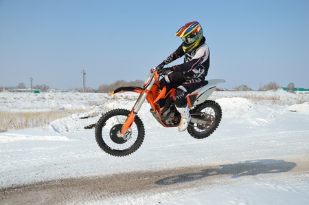 Motocross in the winter, the rider by bike motocross flies sideways over a hill on a snowy road, shot from the left sideの写真素材