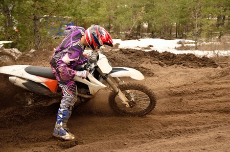 rider bogged down in a deep rut with a large slope of the motorcycle, in a reversal of the loose sandy motocross track, against a background of pine forestの写真素材