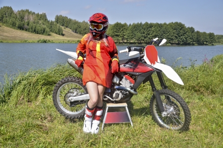 A girl and a motorcycle MX on the green grass near the shore of Lakeの写真素材