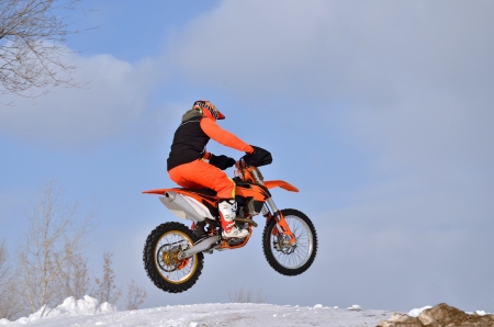 Motorcycling rider on a motorcycle motocross jumps from a hill on a snowy highwayの写真素材