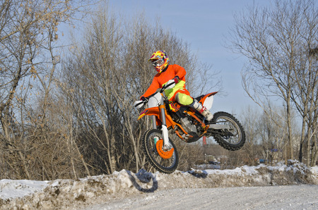 Motorcycling, the rider on the bike for motocross flies over the hill on a snowy highwayの写真素材