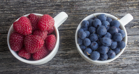 ripe berries - blueberries and raspberries in white cups on a wooden surfaceの写真素材