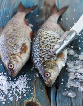 Freshly caught fish on a wooden table and a knife for cleaning of scales