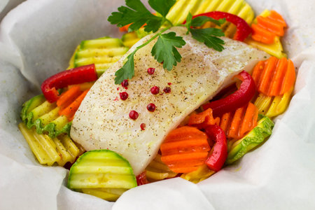A piece of fresh fish fillets with spices and vegetables - potatoes, carrots, zucchini and bell...
