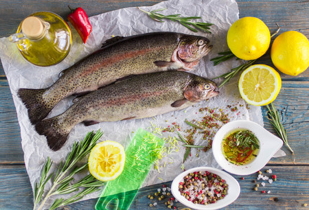 Two fresh rainbow trout with lemon, rosemary and spices on a wooden tableの写真素材