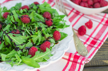 Delicious arugula salad with raspberries and balsamic vinegar in a white plate. Selective focus