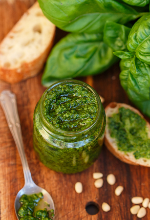 Fresh homemade Basil pesto with pine nuts in a glass jar , Basil leaf and toast on the table. Selective focusの写真素材