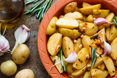 Sliced raw potatoes in a clay baking dish before baking in the oven with spices, garlic, rosemary, olive oil. Dinner in a rustic style. Selective focusの写真素材
