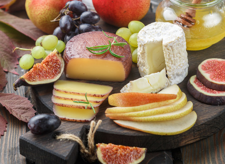 Set of fine cheeses with fruit and honey. Camembert. Bree. Grapes, figs, pears, and rosemary. Wine snacks for foodies. Selective focusの写真素材