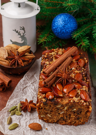 Homemade holiday Fruitcake with nuts, fruits and spices. Almonds, cinnamon, star anise, cardamom on the table. Traditional English pastries. Christmas. New year. Selective focusの写真素材