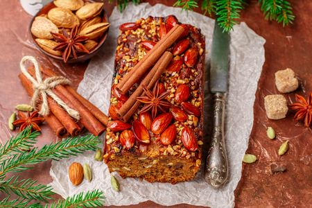 Homemade holiday Fruitcake with nuts, fruits and spices. Almonds, cinnamon, star anise, cardamom on the table. Traditional English pastries. Christmas. New year. Selective focusの写真素材