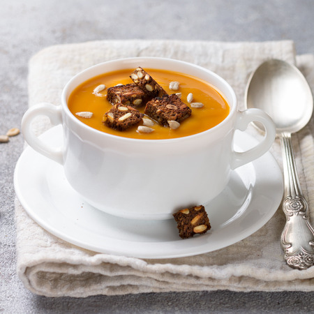 Delicious dietary carrot or pumpkin soup with croutons and sunflower seeds in a white plate. Vegetarian dish. Selective focus and square imageの写真素材