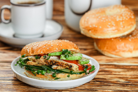 Sesame seeds Whole Grain bagels with chicken grill, Microgreens, cucumber and avocado on white plate on gray background. Healthy breakfast concept . Selective focusの写真素材