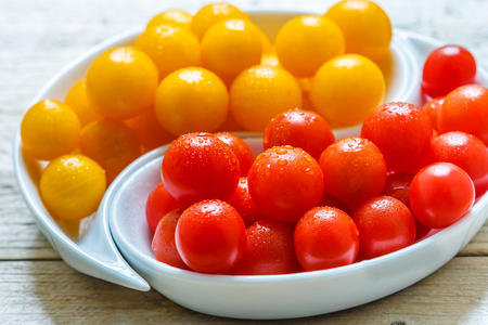 Yellow and red cherry tomatoes with water drops. Fresh and juicy organic vegetables in a white plate on a wooden table. Selective focusの写真素材