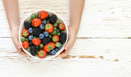 Fresh juicy ripe berries in a white plate in children's hands-strawberries, blueberries,...