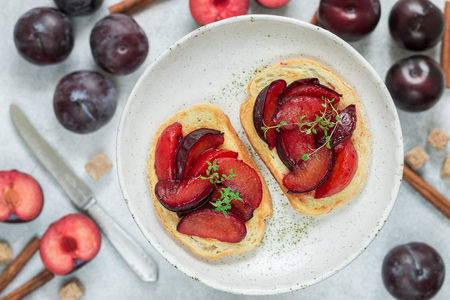 Fruit sweet bruschetta with caramel plums, cinnamon and thyme in a white plate on a gray concrete background. Gourmet Breakfast. Selective focusの写真素材