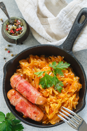 Stewed cabbage with carrots, onions and tomatoes and saucages in bacon with parsley and spices in a cast iron pan. Bigos. Delicious lunch. Selective focusの写真素材