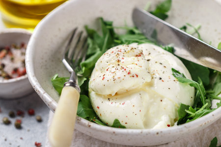 Delicious Creamy Italian Burrata Cheese Served with Olive Oil, fresh arugula and spices in a white...