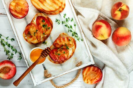 Gourmet summer Breakfast - sandwiches (bread toast, bruschetta) with grilled peaches, cream cheese (ricotta, mascarpone), thyme and honey on an old white wooden table. Selective focusの写真素材