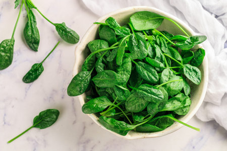 Fresh raw organic spinach leaves with water drops on a white plate on a marble