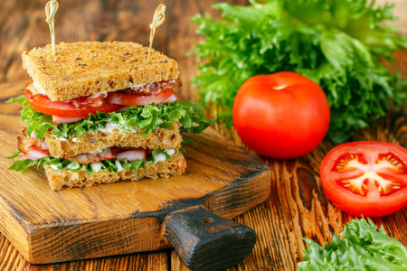 Delicious club sandwiches with green salad lettuce, ham, bacon, fresh tomatoes and sauce on a wooden...