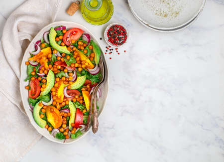 Delicious vegetarian (vegan) salad with chickpeas, avocado, onions, lettuce, colorful yellow and red tomatoes, olive oil and spices. Healthy diet food. Selective focus, top view and copy spaceの写真素材