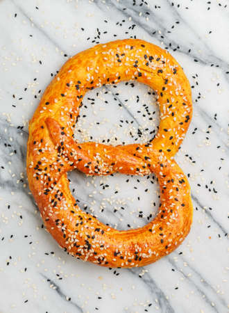 Freshly baked homemade Pretzel with black and white sesame seeds on a marble background. Traditional savory pastries. German (Bavarian) beer appetizer. Selective focusの写真素材