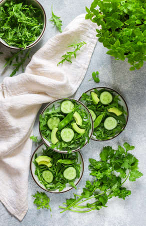 Green vegan or vegetarian salad of fresh vegetables-arugula, cucumber, avocado, green peas, coriander, basil. Three servings on a gray background. Healthy food, diet. top viewの写真素材