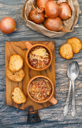 Two servings of traditional French onion soup with baguette and gruyere cheese (emmental, comte or beaufort) in ceramic bowls on a wooden background. Selective focusの写真素材