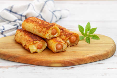 Delicious homemade fried or baked rolls made of wheat bread, sausage and cheese. Gourmet breakfast, brunch. Served on a wooden board with basil. White background. Selective focus, copy spaceの写真素材