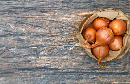 Fresh organic onions in a paper bag on a wooden background. Vegetables from the garden. Bio-products. Selective focus, top view and copy spaceの写真素材