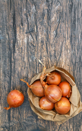 Fresh organic onions in a paper bag on a wooden background. Vegetables from the garden. Bio-products. Selective focus, top view and copy spaceの写真素材