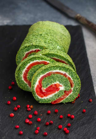 Sliced spinach roll with salted (smoked) red fish (salmon, trout) and cream cheese (ricotta) close-up. roulade. A festive snack for gourmets. Christmas. New Year. Selective focusの写真素材
