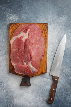 Organic raw pork meat on chopping board ready for cooking. gray concrete or stone background, knife on the table. Close-up, selective focus, top view, copy spaceの写真素材
