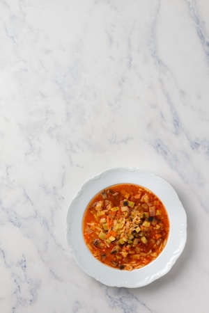 Homemade thick vegetable soup of zucchini, eggplant, carrot, onion, garlic, celery, bell pepper, tomatoes, pasta orzo (risoni), spices. Minestrone. Mediterranean cuisine. Marble background, top viewの写真素材
