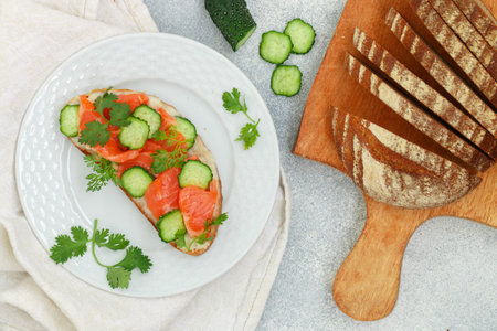 Smorrebrod - traditional Danish sandwich. Black rye bread with salmon, horseradish sauce and fresh cucumber on a white plate on a gray background. delicious snack for gourmets. selective focusの写真素材