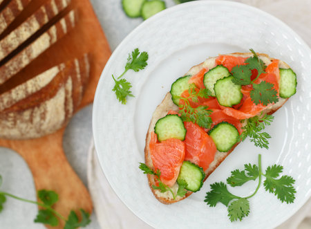 Smorrebrod - traditional Danish sandwich. Black rye bread with salmon, horseradish sauce and fresh cucumber on a white plate on a gray background. delicious snack for gourmets. selective focusの写真素材