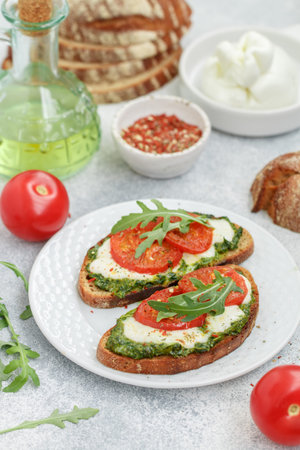 Delicious black rye bread sandwiches with pesto, buratta cheese or mozzarella, tomatoes and fresh arugula. Brunch. Mediterranean cuisine. selective focusの写真素材