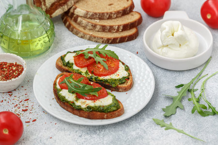 Delicious black rye bread sandwiches with pesto, buratta cheese or mozzarella, tomatoes and fresh arugula. Brunch. Mediterranean cuisine. selective focusの写真素材