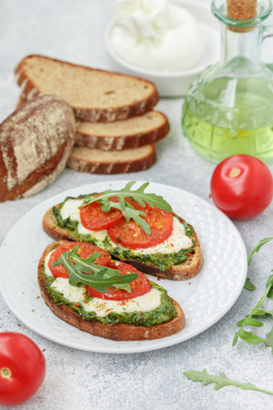 Delicious black rye bread sandwiches with pesto, buratta cheese or mozzarella, tomatoes and fresh arugula. Brunch. Mediterranean cuisine. selective focusの写真素材