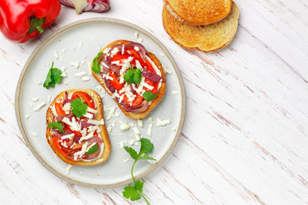 Buscetta with roasted red bell pepper, onion, feta cheese, cilantro and spices. Breakfast. Brunch. Grey plate, white wooden table. Selective focus, top view and copy spaceの写真素材