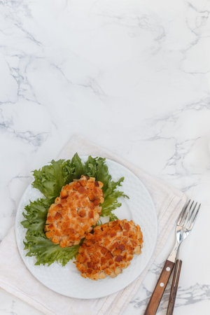 Pozharsky cutlets and lettuce leaf in a white plate on a marble background. Selective focus, top view, place for textの写真素材