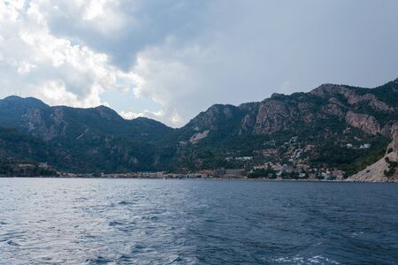 Calm dark blue sea and sky with a mountains and small town in the backgroundの写真素材