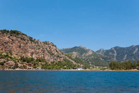 View from the sea on a tourist village on the background of a brown mountainの写真素材