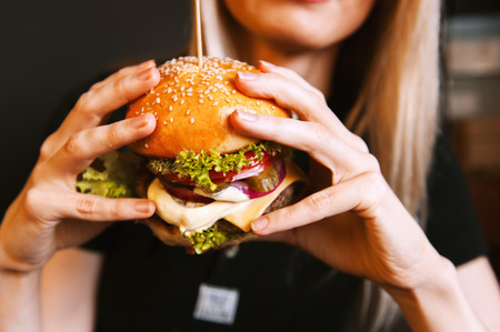 beautiful young, healthy girl holds a tasty big burger with beef cutlet. the concept of nourishing food.の写真素材