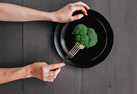 broccoli in a black plate on a wooden table. cutlery. healthy eating concept