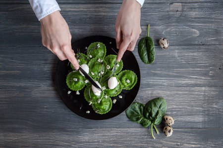 delicious green ravioli with the addition of spinach dough, stuffed with ricotta and porcini mushrooms. poached quail egg, blue cheese. on a black plate on a wooden background.の写真素材