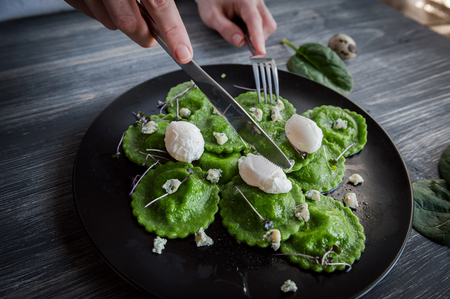 delicious green ravioli with the addition of spinach dough, stuffed with ricotta and porcini mushrooms. poached quail egg, blue cheese. on a black plate on a wooden background.の写真素材