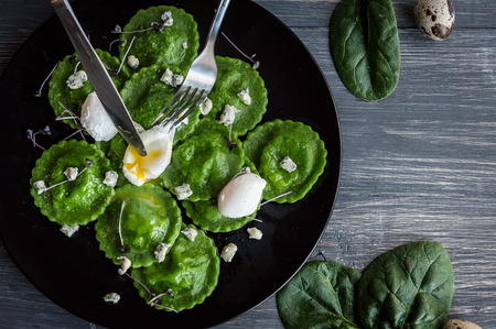 luxurious meal in a restaurant. delicious green ravioli with the addition of spinach dough, stuffed with ricotta and porcini mushrooms. poached quail egg, blue cheese. on a black plate on a wooden background.の写真素材