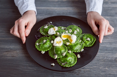 luxurious meal in a restaurant. delicious green ravioli with the addition of spinach dough, stuffed with ricotta and porcini mushrooms. poached quail egg, blue cheese. on a black plate on a wooden background.の写真素材